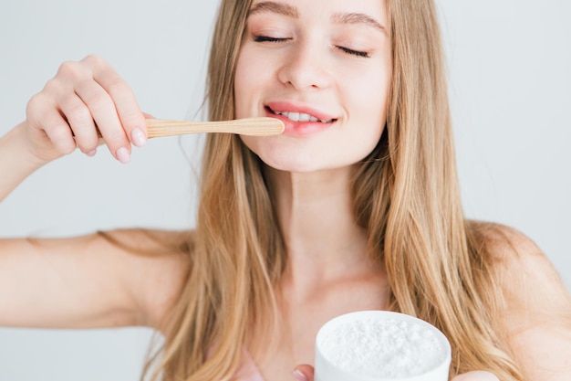 Young beautiful girl holding a useful bamboo toothbrush and a jar of tooth powder. The concept of a healthy lifestyle, environmental friendliness and zero waste. Toning.