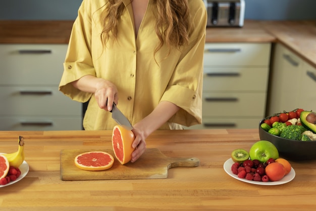 Young beautiful girl is cutting a grapefruit. A woman prepares a delicious and healthy fruit salad.