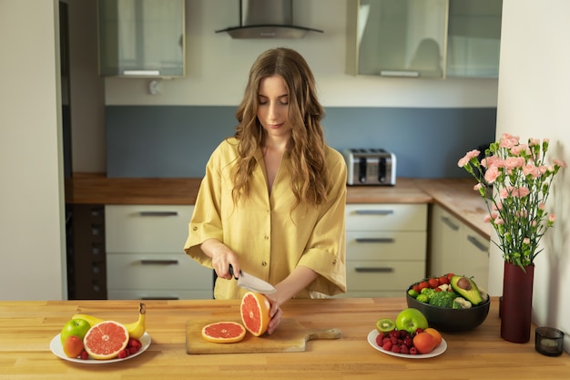 Young beautiful girl is cutting a grapefruit. A woman prepares a delicious and healthy fruit salad.