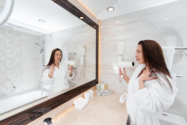 A young beautiful girl is drying her hair in a beautiful white bathroom A fresh good morning at the hotel Rest and travel Hotel recreation and tourism