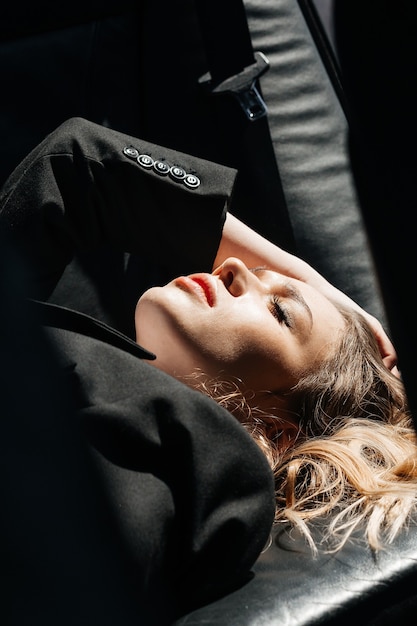 A young, beautiful girl is lying in the back seat of a car. Large portrait of a girl.