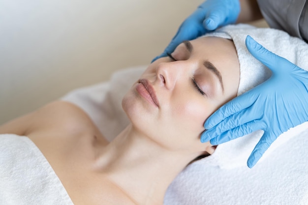 A young beautiful girl lies on the table at the beautician and receives procedures, a light massage, hands in blue gloves, the skin is smooth