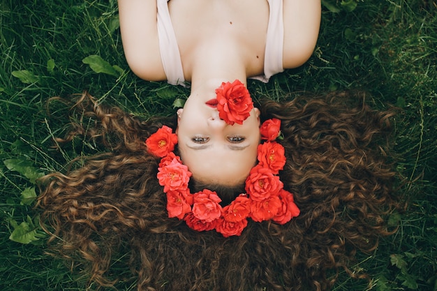 Young beautiful girl lying at the grass with flowers wreath