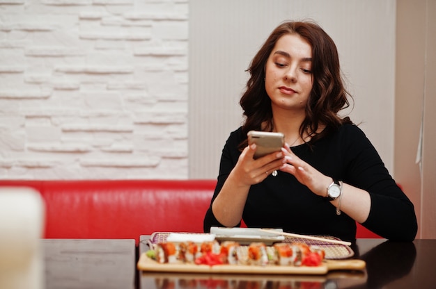 A young beautiful girl making photo by phone of sushi on traditional Japanese restaurant.