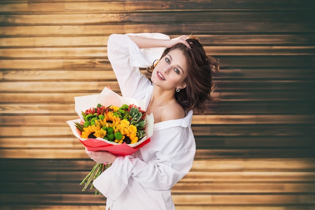 Young beautiful girl model with bouquet of flowers on wooden background