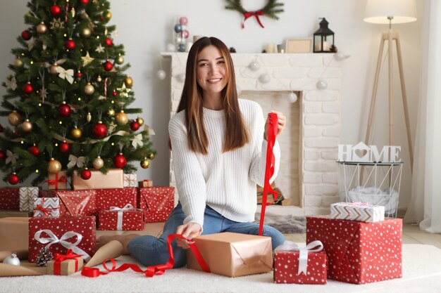 Young beautiful girl packing christmas gifts in decorated home interior