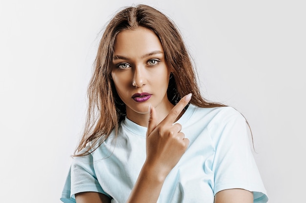 Young beautiful girl pointing finger to the side at on a white isolated background. A woman points to an idea, a place for advertising. Serious girl with fashion make-up with purple lips.