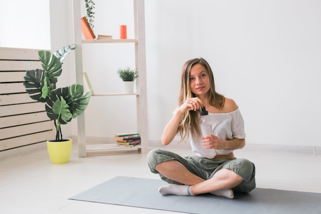 Young beautiful girl practicing yoga at mat drinking water while break fitness and healthy lifestyle