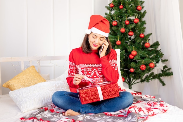 A young beautiful girl in a red sweater and a hat is making a video call with a gift