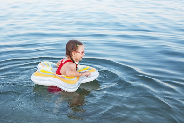 Young beautiful girl in a red swimsuit swims on a rubber ring on the sea