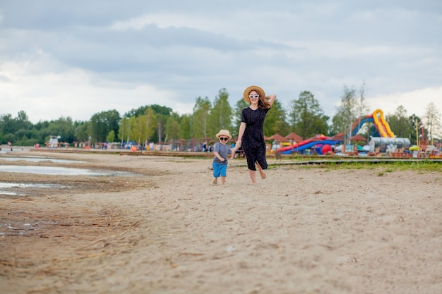 A young beautiful girl runs along a sandy beach in the sea with her son.