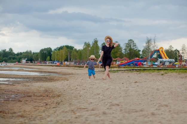 A young beautiful girl runs along a sandy beach in the sea with her son