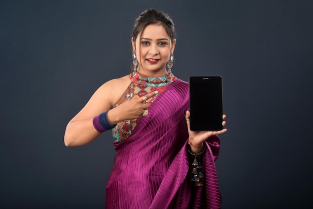 Young beautiful girl showing a blank screen of smartphone or mobile or tablet phone on a grey background