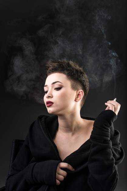 Young beautiful girl sitting in chair and smoking against the dark background