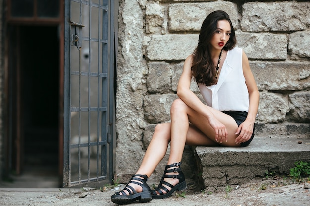 Young and beautiful girl sitting at the door on a stone slab