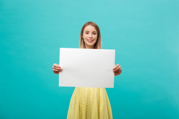 young beautiful girl smiling and holding a blank sheet of paper, dressed in yellow