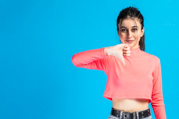 Young beautiful girl standing on blue background and gesture thumb down