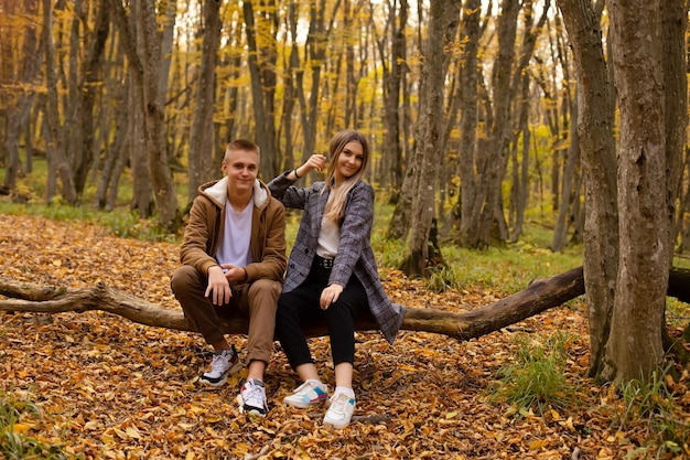 a young beautiful girl stands behind a guy sitting on a fallen tree in the autumn city forest