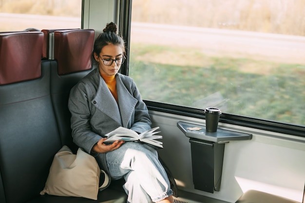 Young beautiful girl on a train reading a book while traveling in a train.