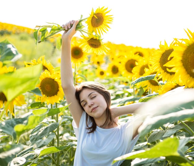 Young beautiful girl walks in the summer in a field with blooming sunflowers