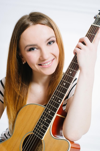 Young beautiful girl wearing jeans and a striped Tshirt with an acoustic guitar on a white background