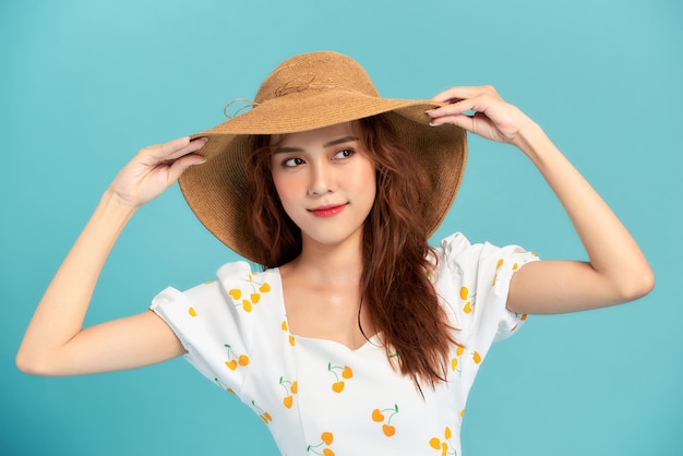 Young beautiful girl wearing a straw hat stands and smiles isolated over blue background