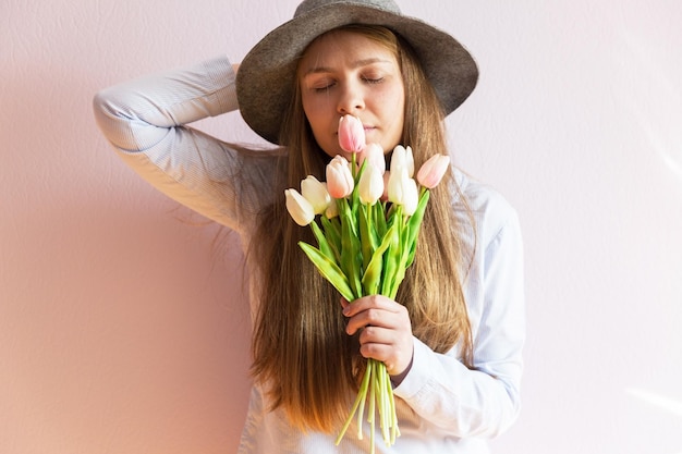 A young beautiful girl with blond dissolved long hair a felt hat on her head keeps spring flowers