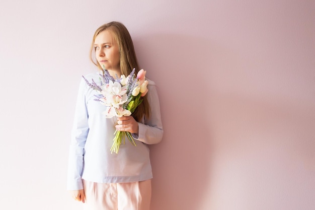 A young beautiful girl with blond dissolved long hair a felt hat on her head keeps spring flowers