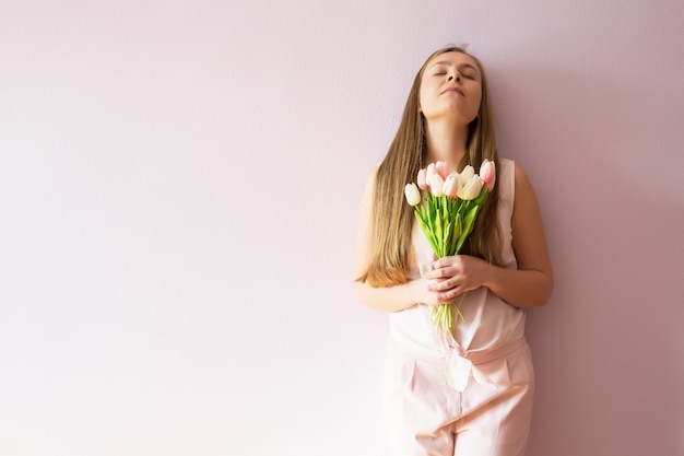 A young beautiful girl with blond dissolved long hair a felt hat on her head keeps spring flowers