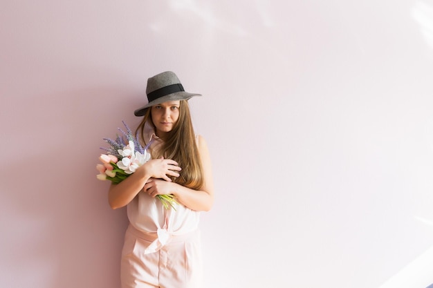 A young beautiful girl with blond dissolved long hair a felt hat on her head keeps spring flowers