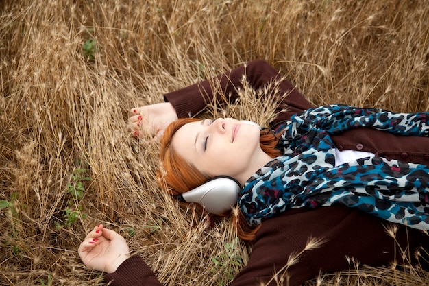 Young beautiful girl with headphone lying down at outdoor. Autumn season time yellow grass on background