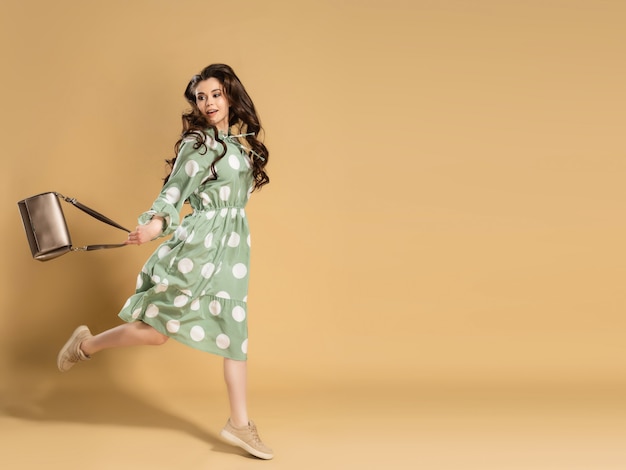 A young beautiful girl with long curly hair in a dress with polka dots is jumping with a bag in her hands on an orange.