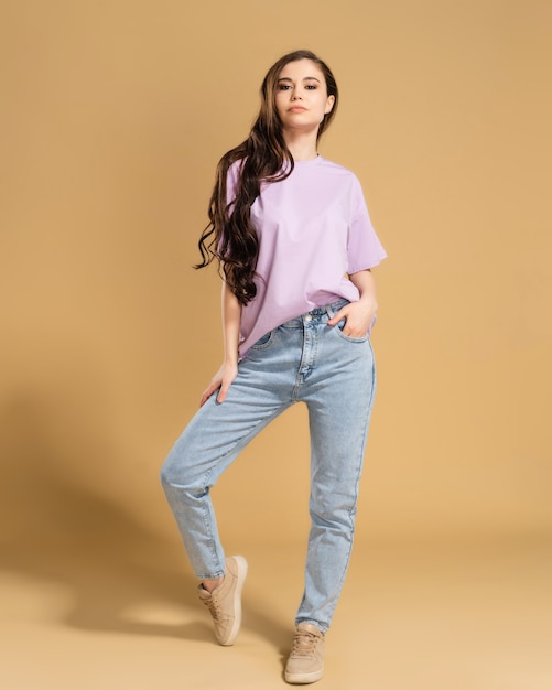 Young beautiful girl with long curly hair in a lilac T-shirt and blue jeans on a pastel orange.