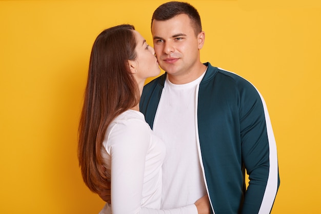 Young beautiful girl with long dark hair kissing her handsome boyfriend to cheek