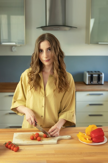 Young beautiful girl with long hair slices cherry tomatoes. A woman prepares a salad of natural, fresh and healthy vegetables.