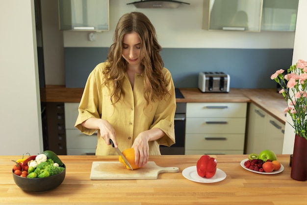 Young beautiful girl with long hair slices sweet pepper. A woman prepares a salad of fresh, healthy vegetables.