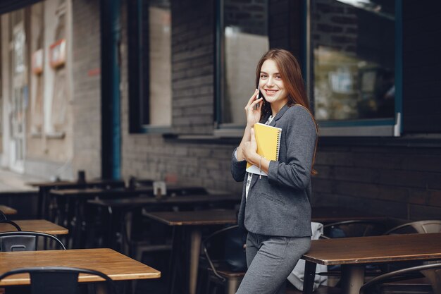 young and beautiful girl with notebook standing near building in a city and use the phone