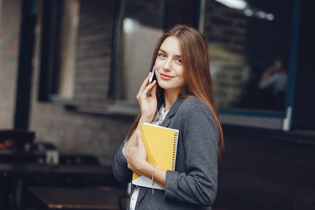 young and beautiful girl with notebook standing near building in a city and use the phone