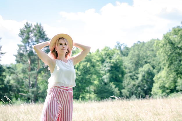 Young beautiful girl with pink hair in the summer hat on the glade