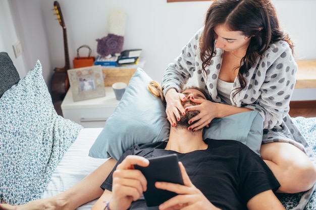 Young beautiful happy couple in love lying on bed cuddling using tablet