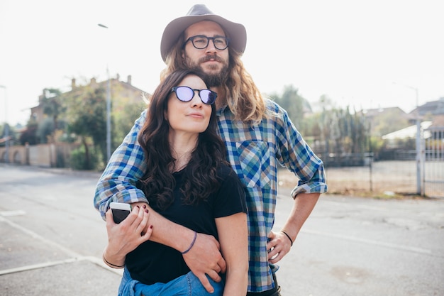 Young beautiful happy couple outdoor hugging holding smartphone