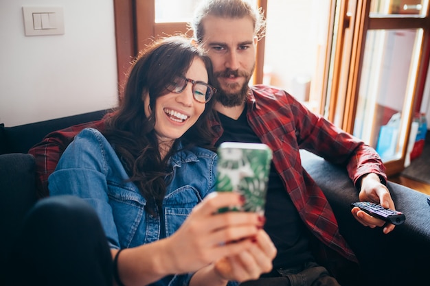 Young beautiful happy couple sitting couch indoor home taking selfie