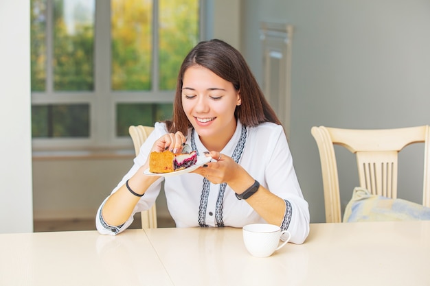 Young beautiful happy girl having Breakfast coffee and cheesecake sitting at the table