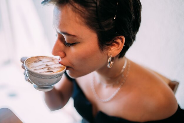 Young beautiful happy Latin woman enjoying cappuccino in a street cafe