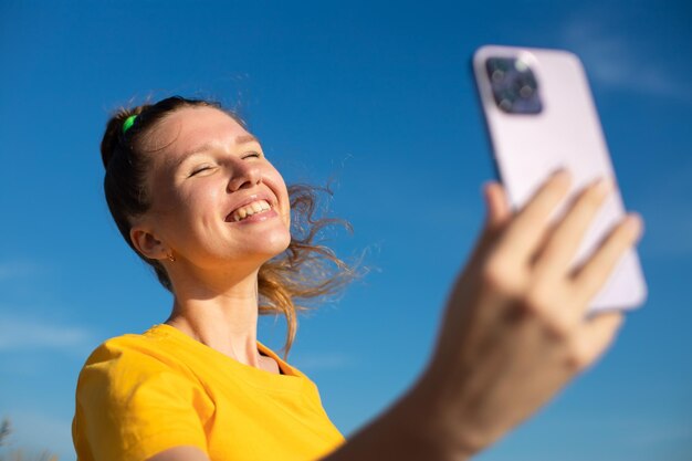 Young beautiful happy woman blogger is taking selfie picture of herself on frontal camera to social media of smartphone cell mobile phone smiling waving her hand having video call conversation