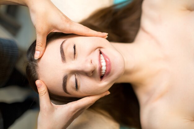 Young beautiful happy woman receiving head face massage in beauty spa