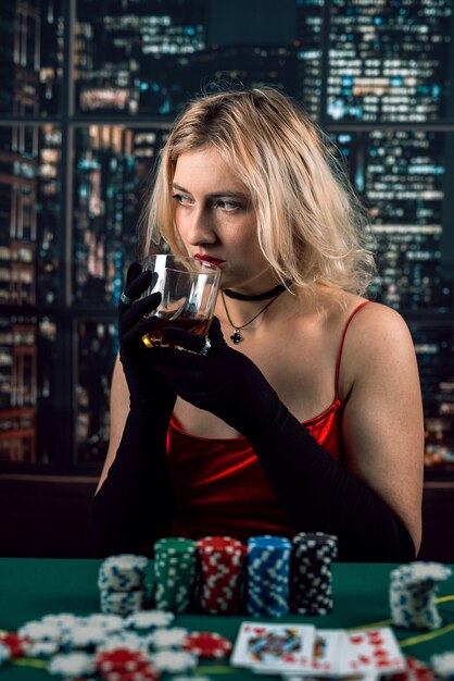 young beautiful happy woman in a red evening dress holds her cards a pair of aces and chips on a green background playing poker in a casino a woman in a red dress