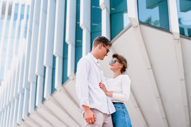 Young beautiful hipster couple in sunglasses in love walking on modern city street