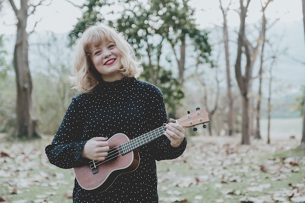 Young beautiful hipster woman in the park playing ukulele and smilling.Vintage tone