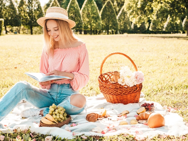 Young beautiful hipster woman in trendy summer jeans, pink T-shirt and hat. Carefree woman making picnic outside. 